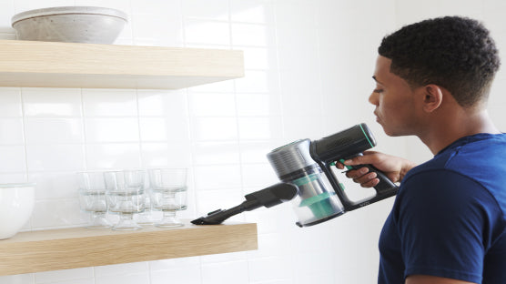 Person using cordless vacuum to vacuum shelf